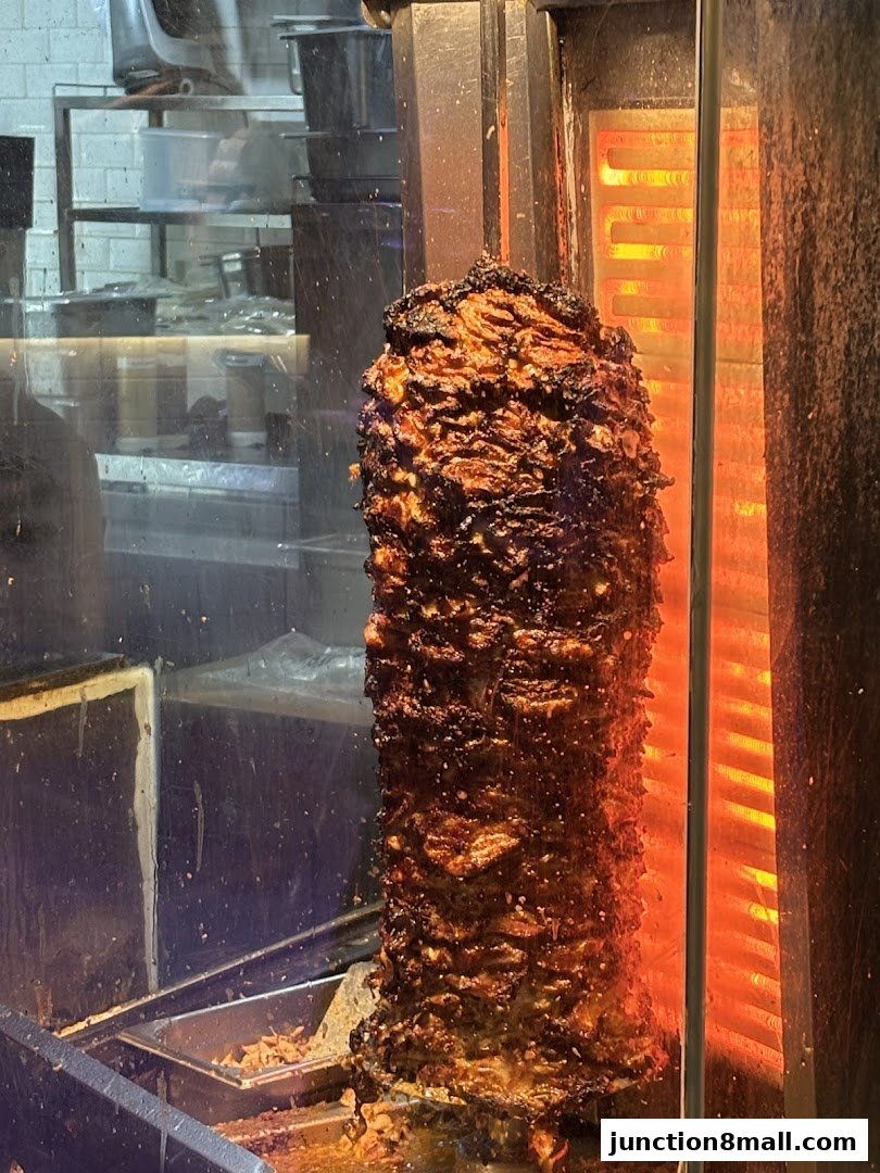 A vertical rotisserie spit of seasoned meat cooking in front of glowing heating elements.