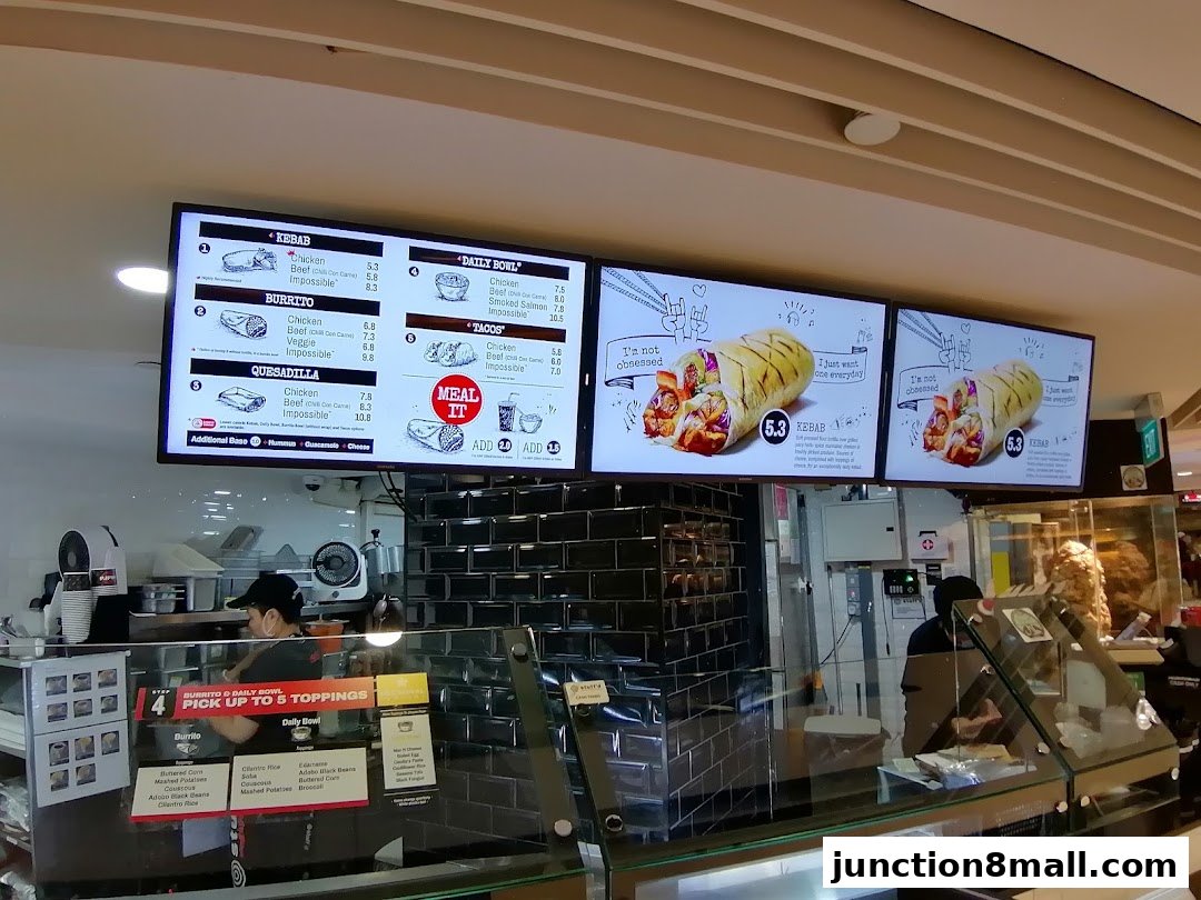Digital menu boards displaying kebabs, burritos, quesadillas, tacos, and daily bowls at a food stall.