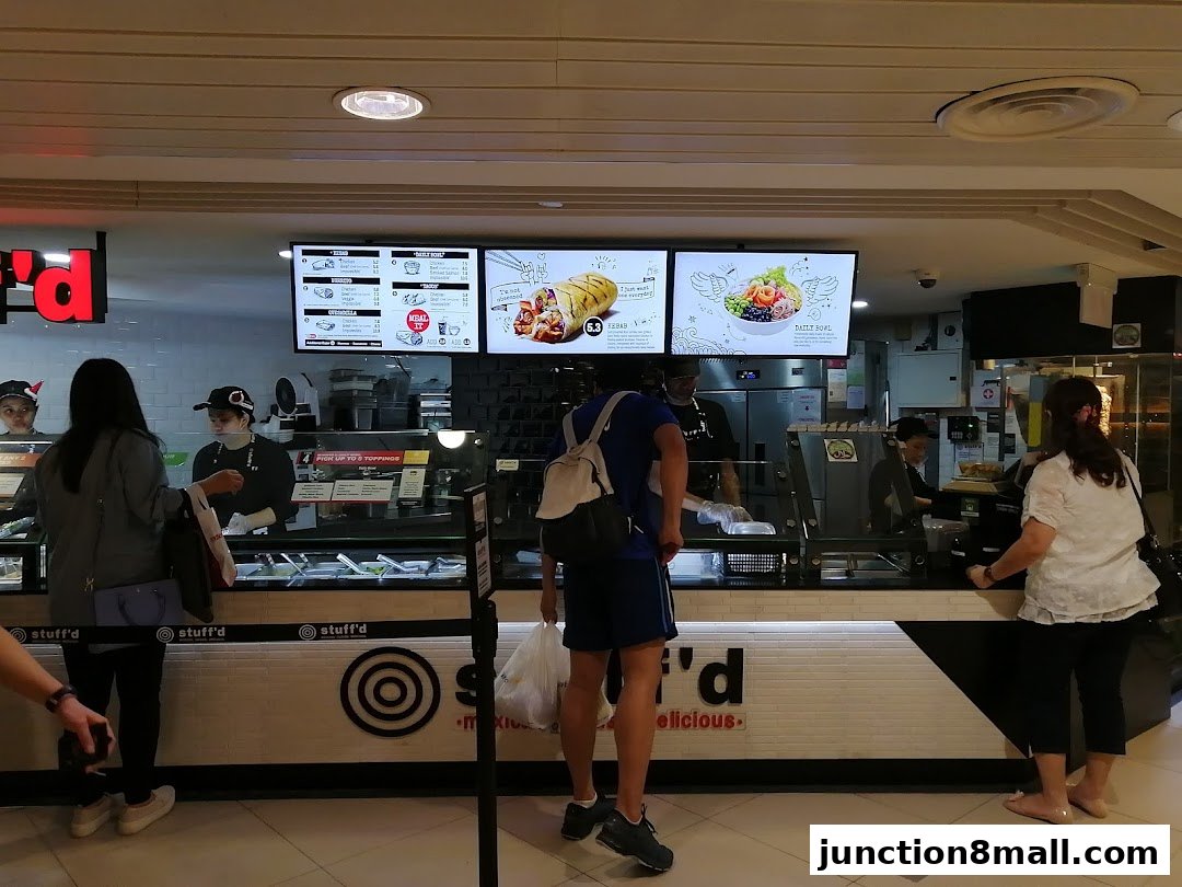 Customers ordering food at a counter with digital menus displaying food options.