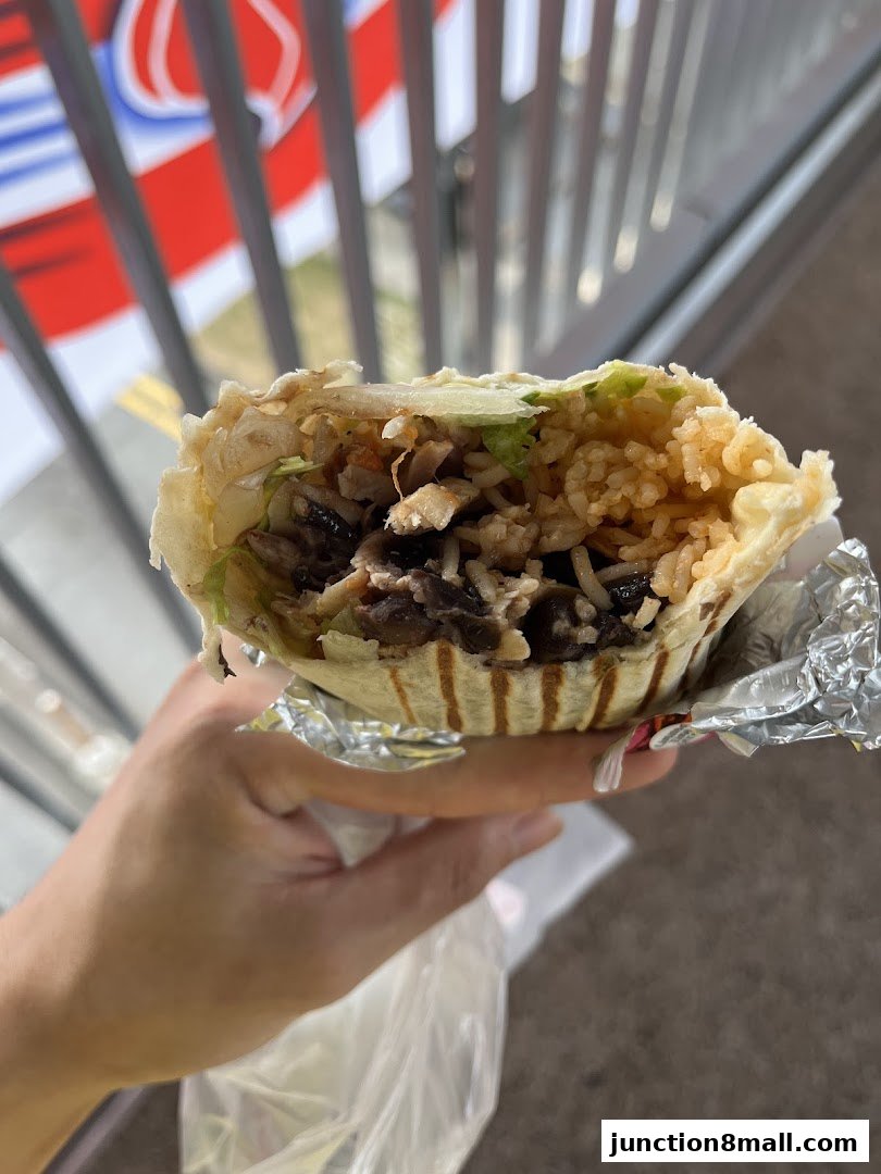 A hand holds a large, foil-wrapped burrito filled with rice, beans, and other ingredients.