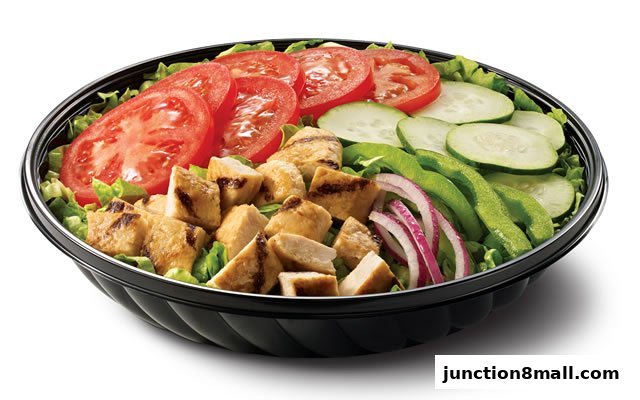 A fresh salad with grilled chicken, tomatoes, cucumbers, bell peppers, and red onions in a black bowl.