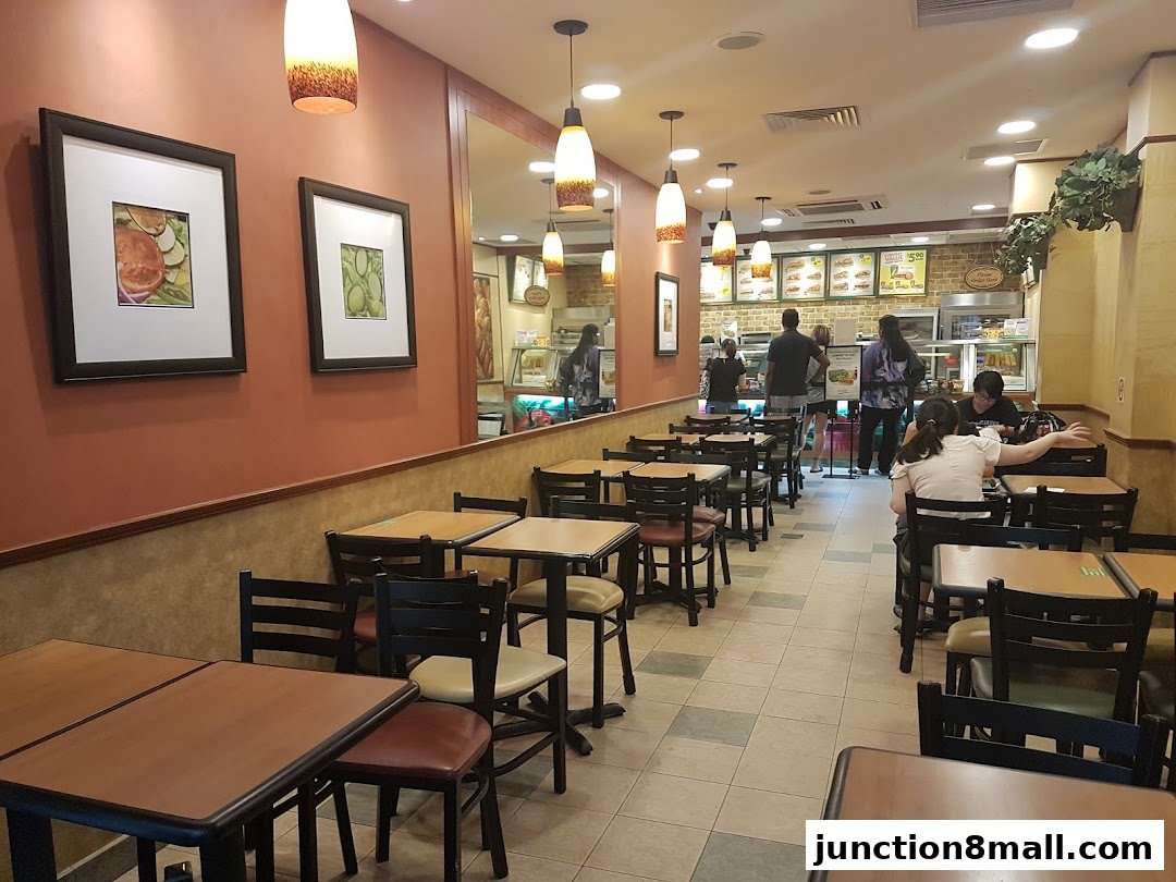 Interior view of a Subway restaurant with tables, chairs, and customers at the counter.
