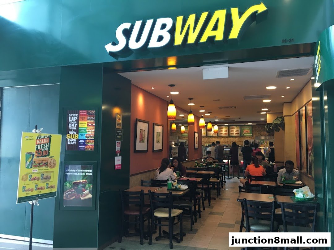 The entrance to a Subway restaurant with seating and customers inside.