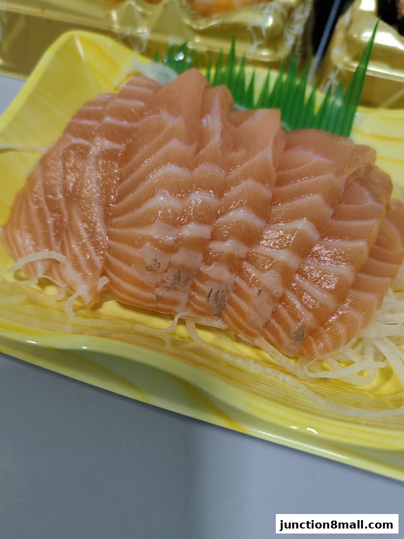 A close-up of fresh salmon sashimi served on a yellow tray with shredded daikon.
