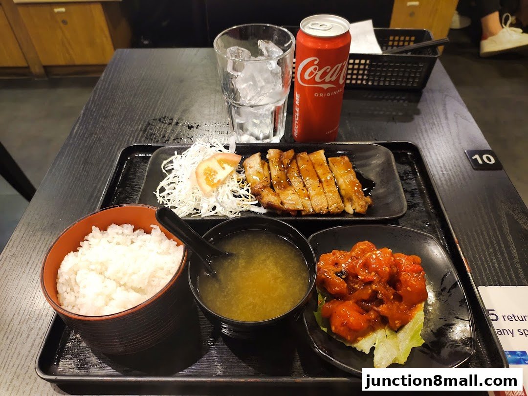 A Japanese meal set with grilled meat, rice, soup, and a side dish, served with a drink.