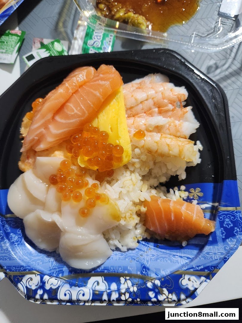 A close-up of a sushi bowl with salmon, shrimp, scallops, and ikura on rice.