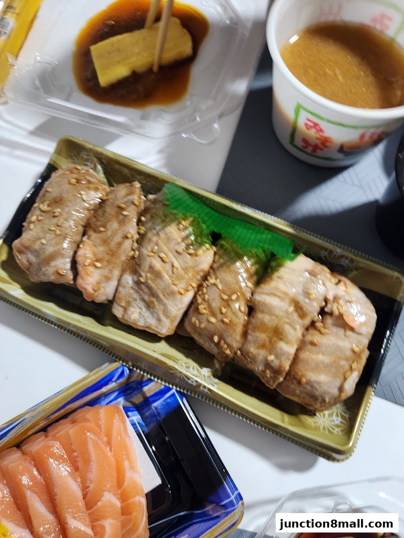 A close-up of a Japanese meal featuring salmon sashimi, grilled meat, and miso soup.