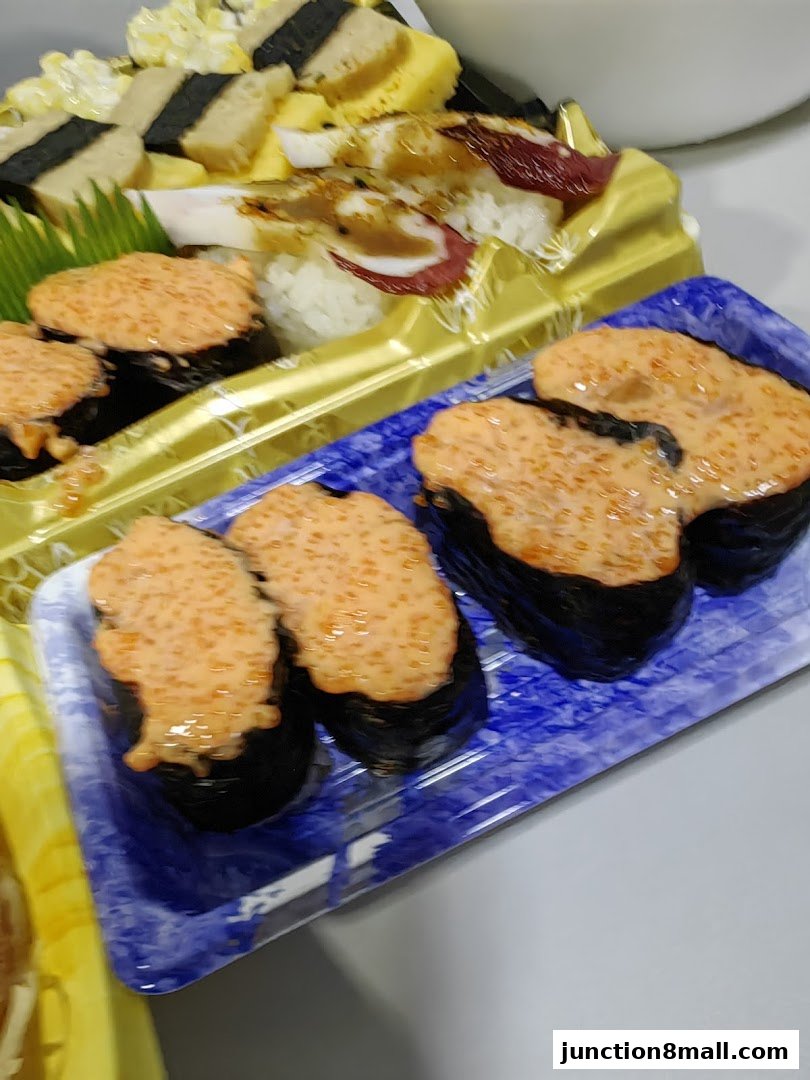 A close-up of various sushi dishes, featuring gunkan maki with orange topping and other sushi rolls.