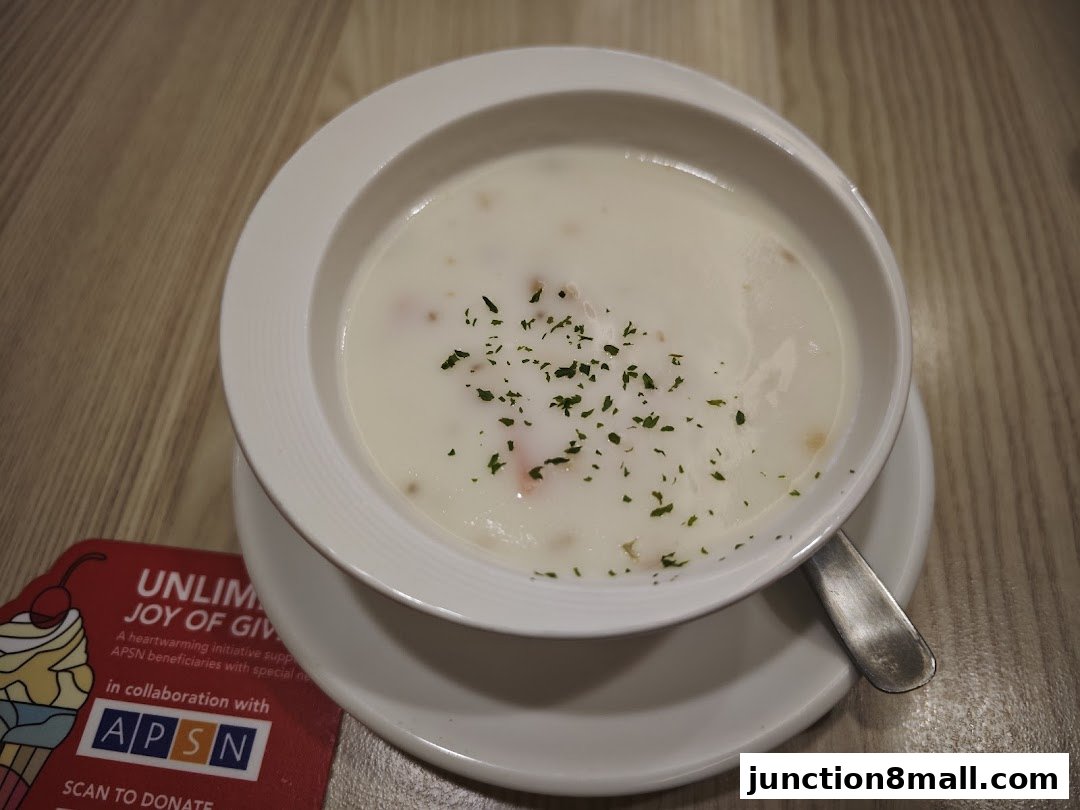 A bowl of creamy soup topped with herbs and a spoon rests on a saucer.