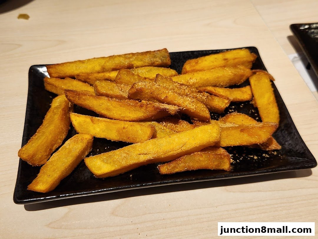 A black rectangular plate filled with golden-brown, seasoned potato wedges.
