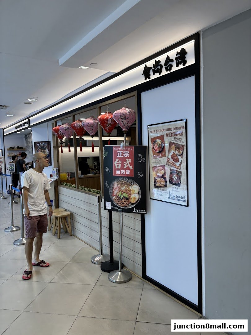 A man stands outside a Taiwanese restaurant with decorative lanterns and a menu display.