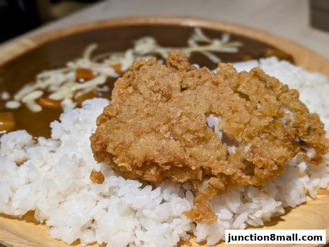 A close-up of a crispy fried chicken cutlet served over fluffy white rice with curry sauce.