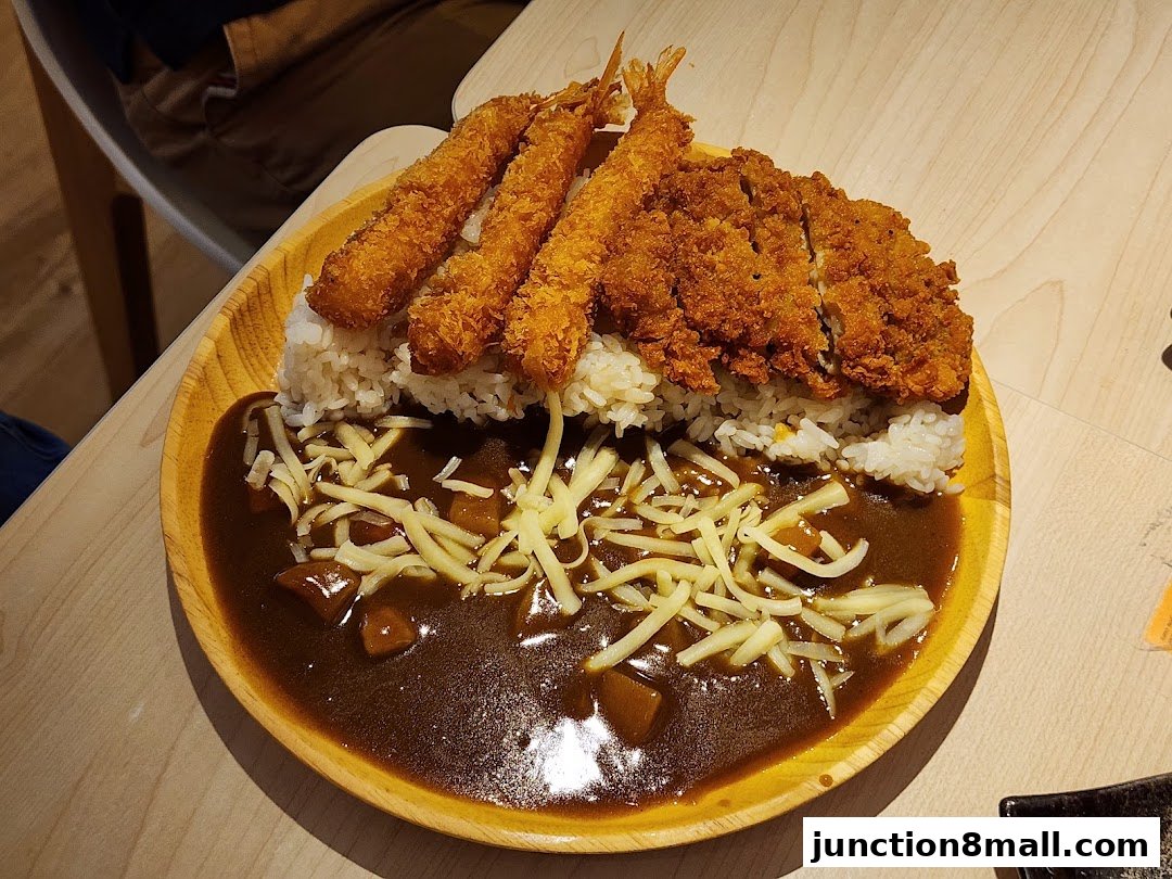 A plate of Japanese curry with rice, fried chicken, and shrimp, topped with shredded cheese.