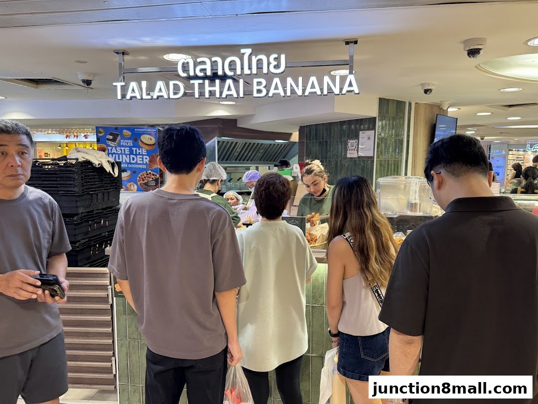 Customers queue at Talad Thai Banana, a food stall with a bright sign and green tiled background.