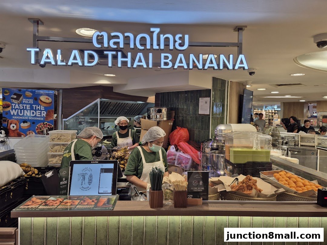 A food stall with staff preparing food behind a counter, featuring a prominent sign.