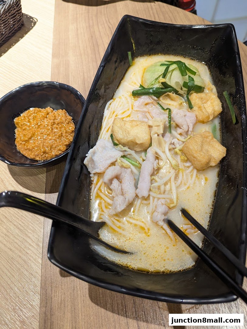 A bowl of delicious-looking noodle soup with meat and vegetables, served with a side of chili paste.