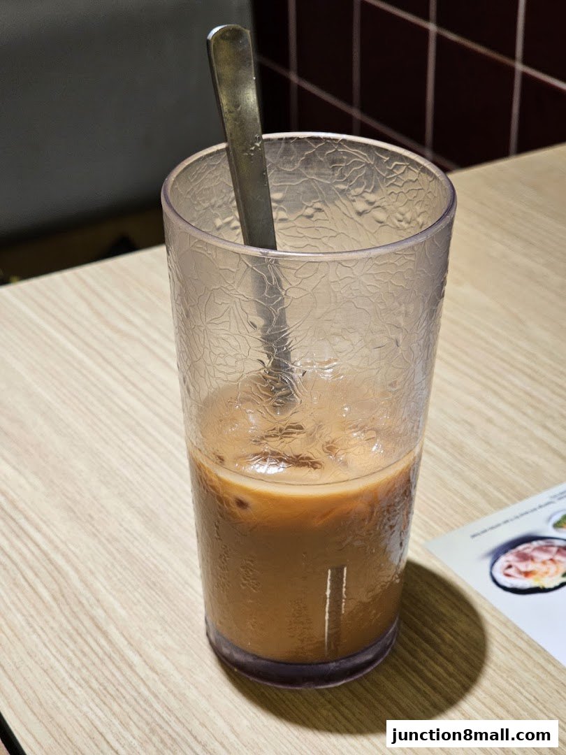 A close-up of an iced milk tea with a spoon in a textured glass on a wooden table.