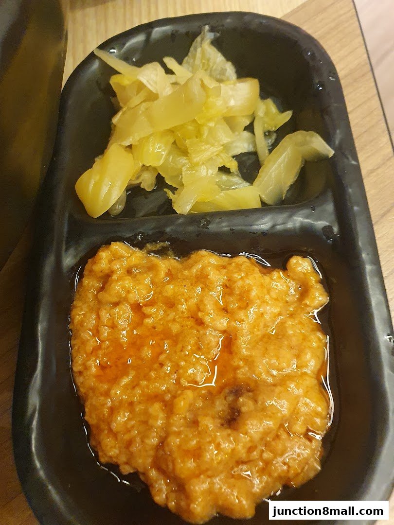 A close-up of a black divided dish containing pickled vegetables and a spicy sauce.