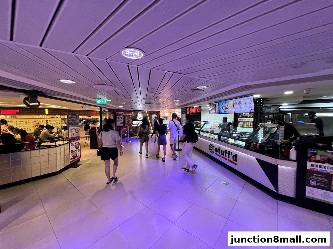 People walking past a food stall with a display of food and a menu board.