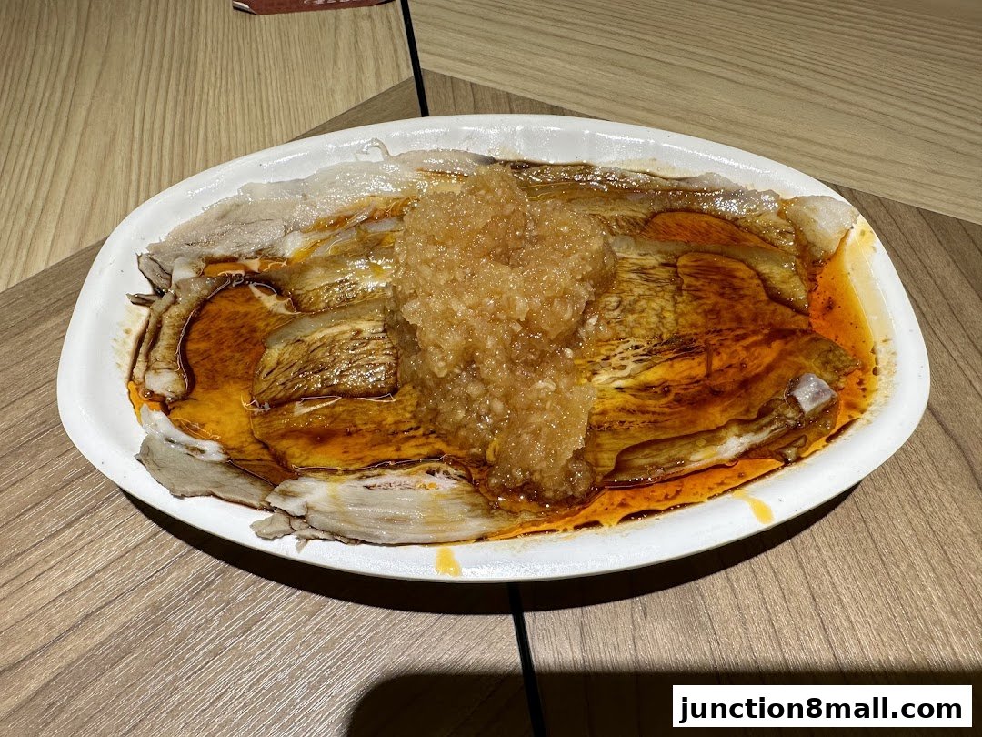 A plate of sliced meat with sauce and minced garlic on a wooden table.