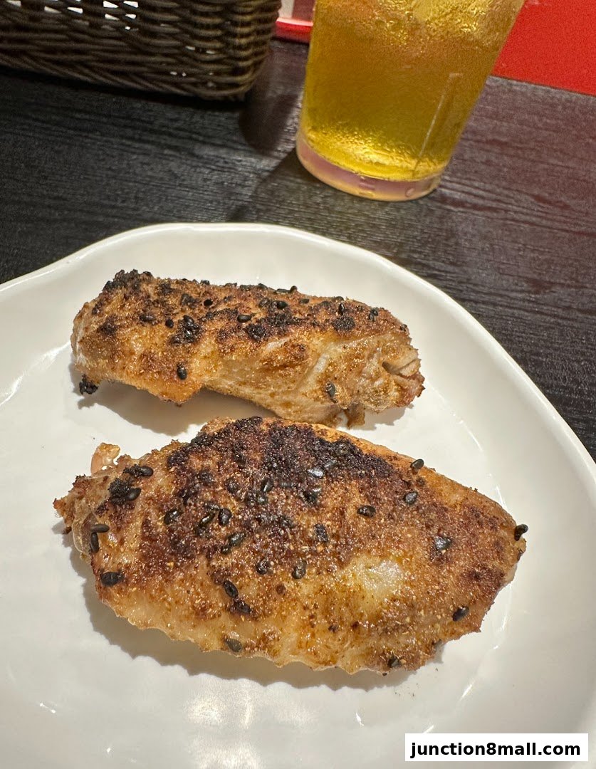 Two pieces of seasoned chicken wings served on a white plate with a drink in the background.