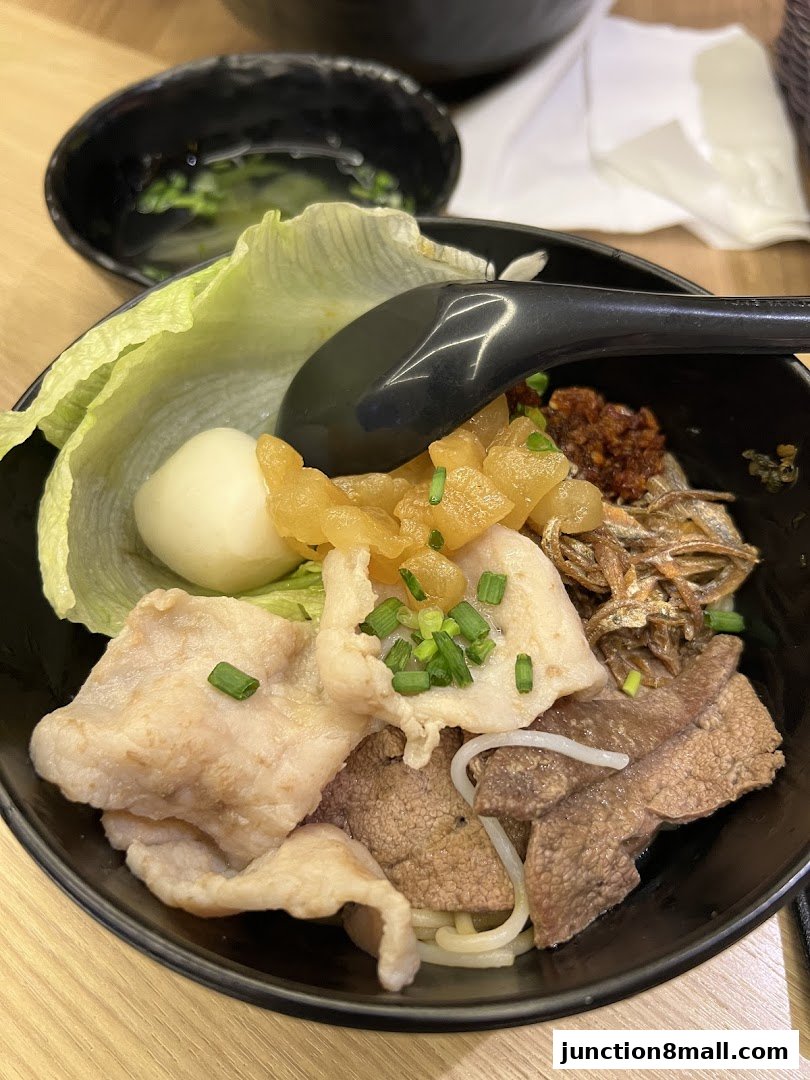 A close-up of a delicious bowl of mixed noodles with various toppings and a side of soup.
