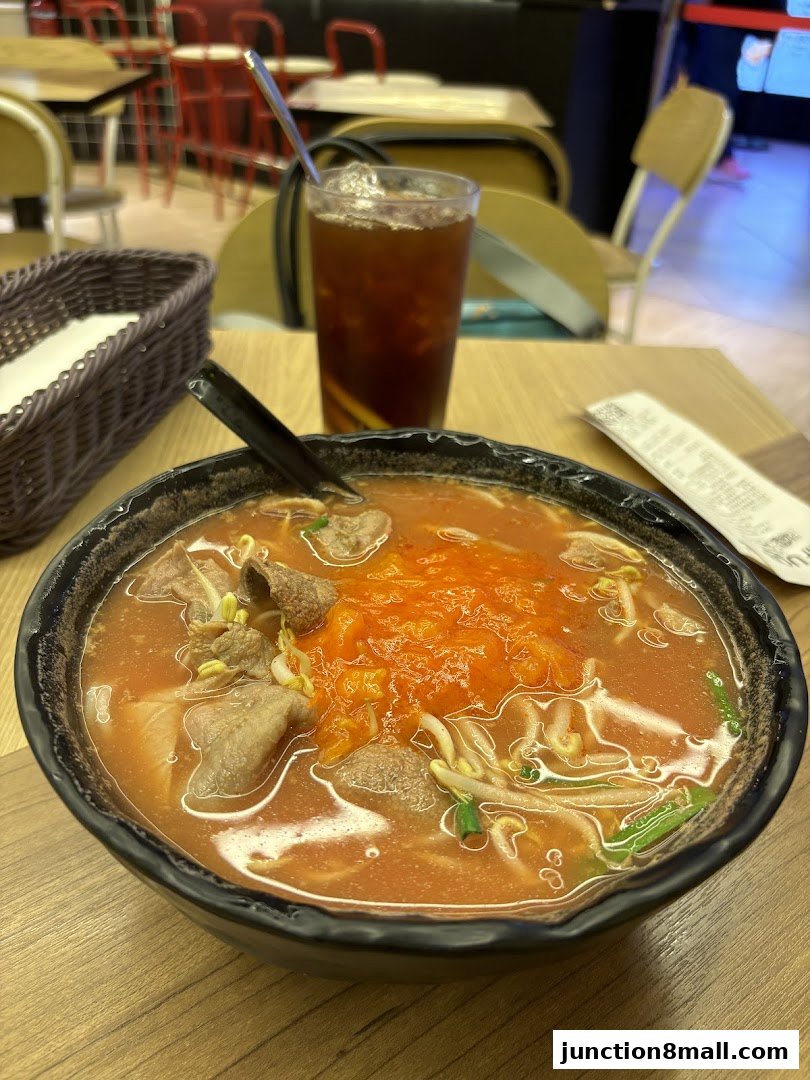 A close-up of a bowl of noodle soup with meat and bean sprouts, and a glass of iced tea.