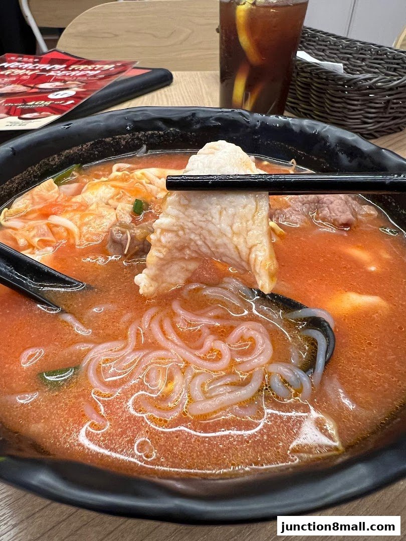 A close-up of a steaming bowl of noodle soup with meat and vegetables, and a drink.
