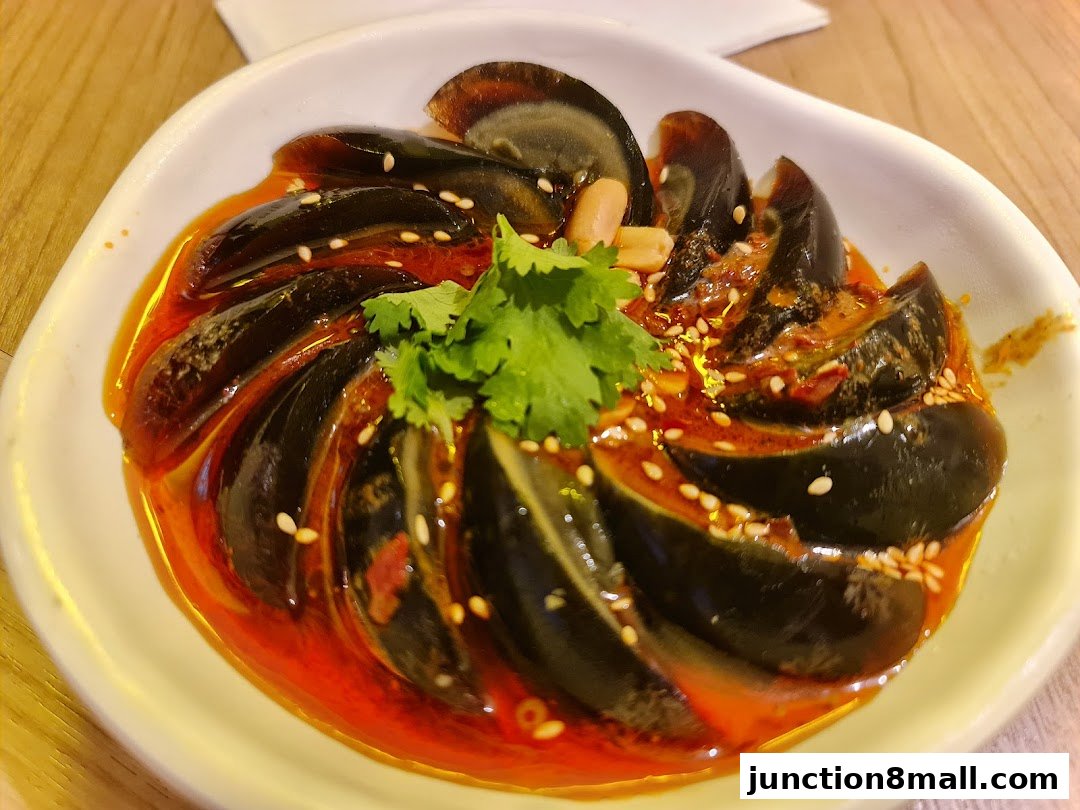 A plate of century eggs served with chili oil, sesame seeds, and cilantro.