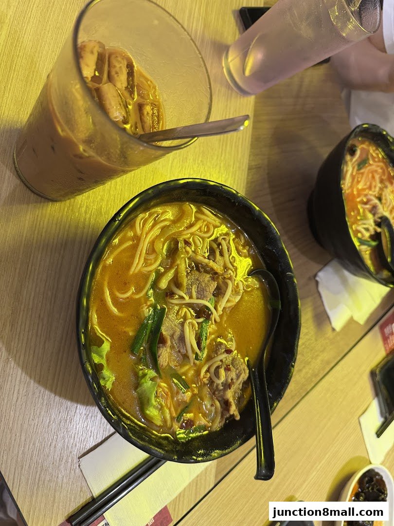 A close-up overhead view of two bowls of noodle soup and a drink on a wooden table.