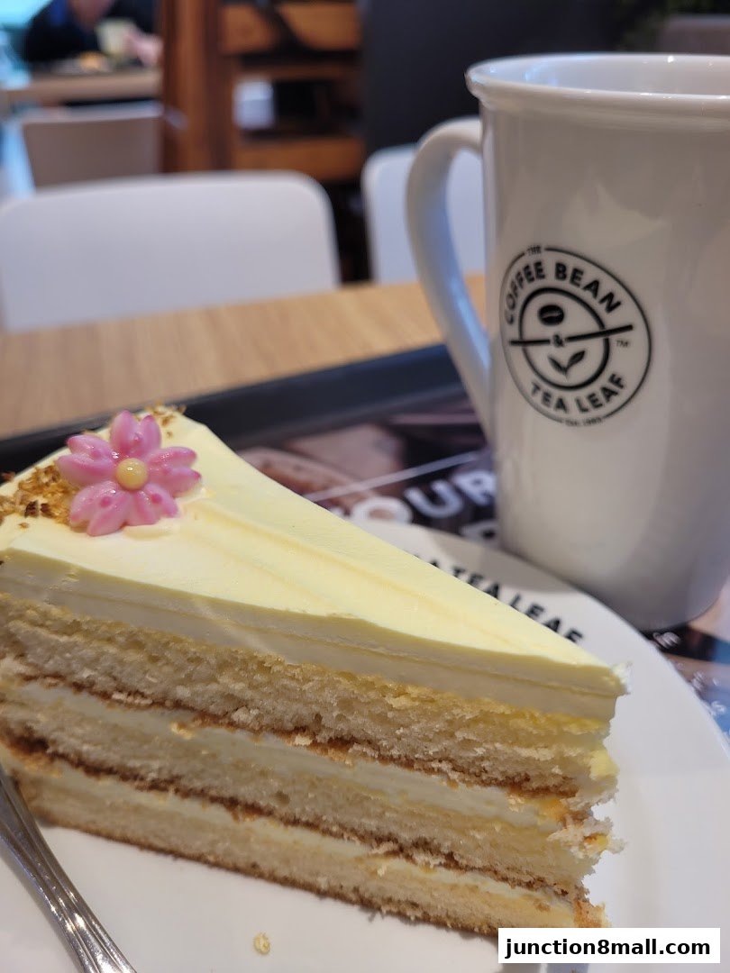 A slice of layered cake with a pink flower decoration and a mug with the Coffee Bean logo.
