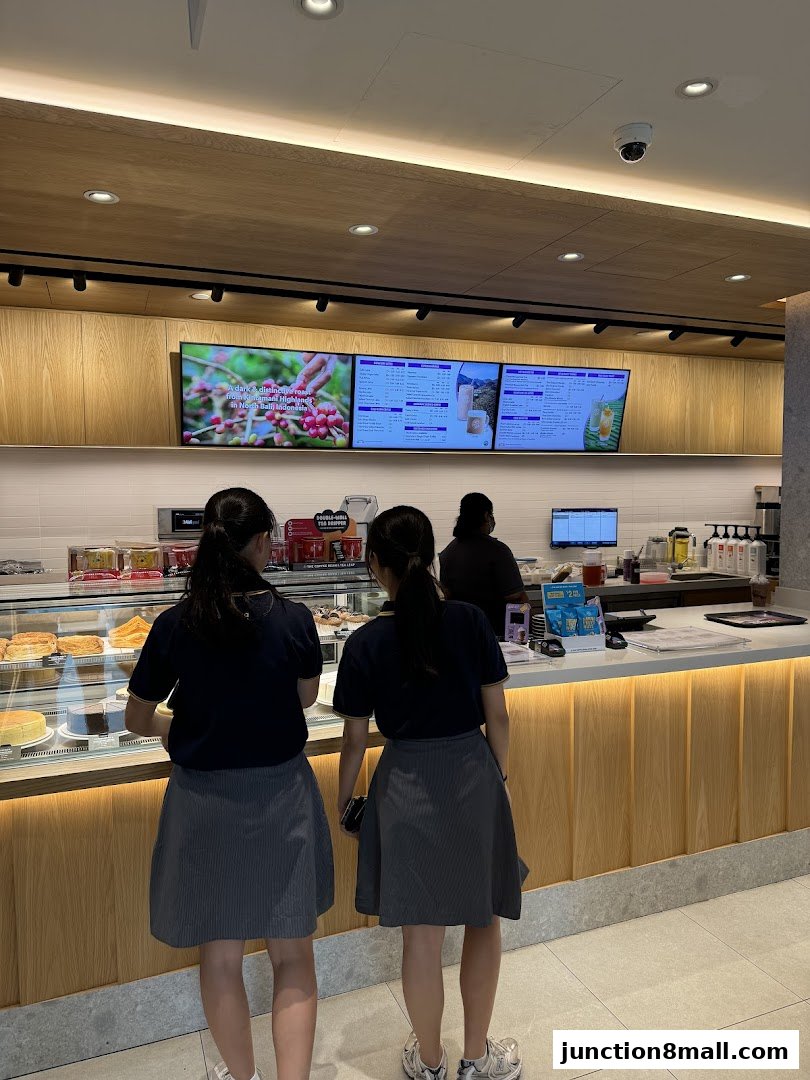 Two students stand at a counter in a coffee shop, looking at the menu.