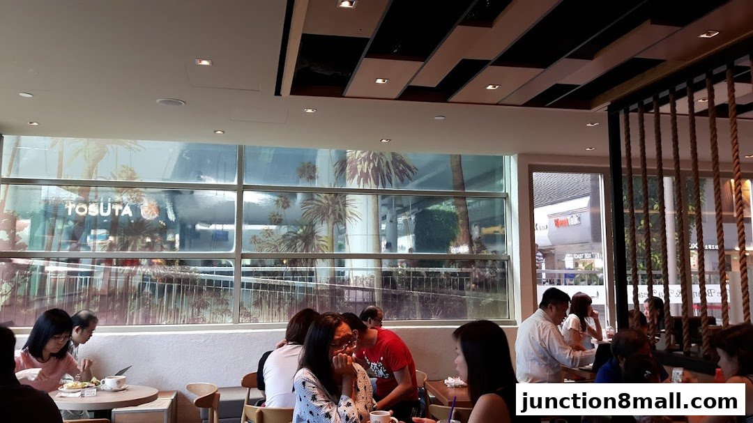 People enjoying coffee and tea inside a cafe with a view of palm trees through the window.