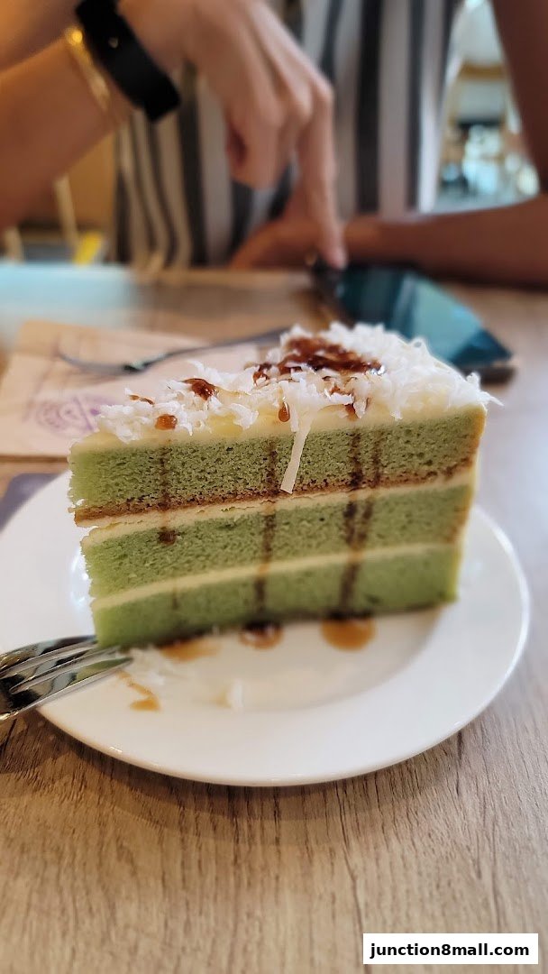 A slice of layered green cake with white frosting and shredded coconut on a white plate.