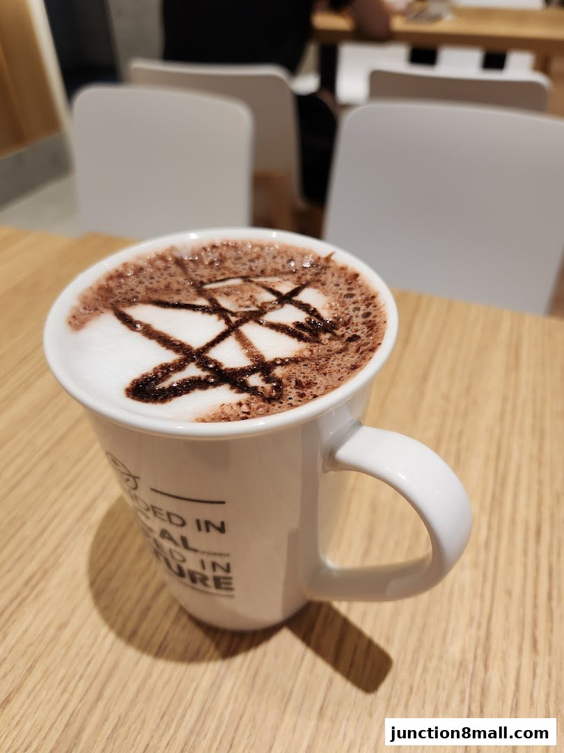 A close-up of a hot chocolate with latte art in a white mug on a wooden table.