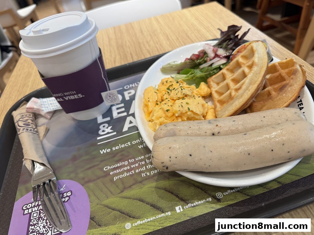 A breakfast platter with scrambled eggs, waffles, sausages, and a side salad, served with a coffee cup.