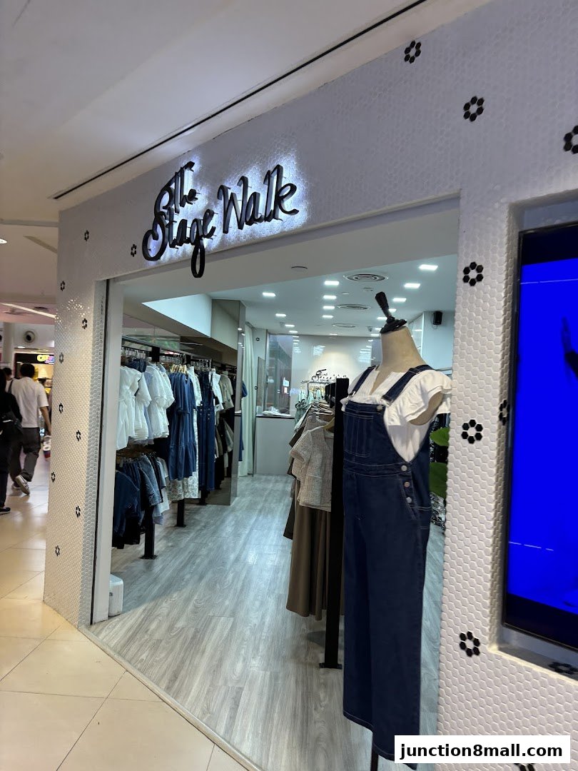The entrance of 'The Stage Walk' clothing store, featuring a mannequin in denim overalls and racks of apparel.