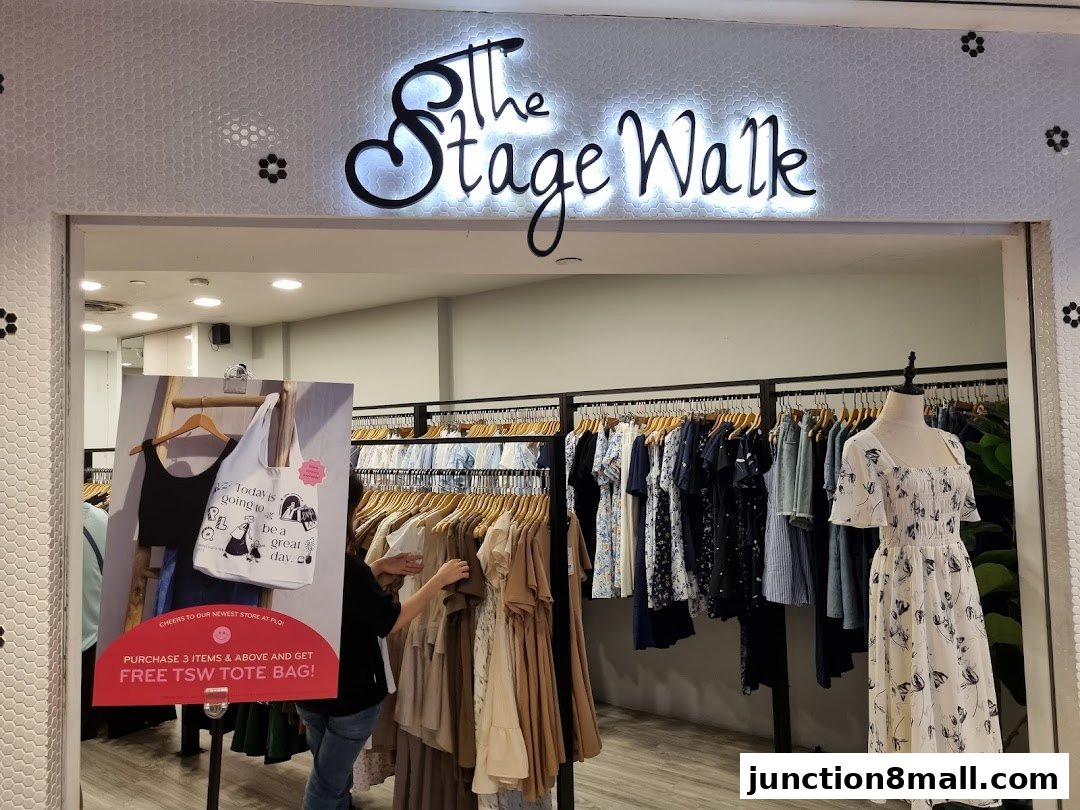 The Stage Walk clothing store entrance with racks of apparel and a promotional sign.