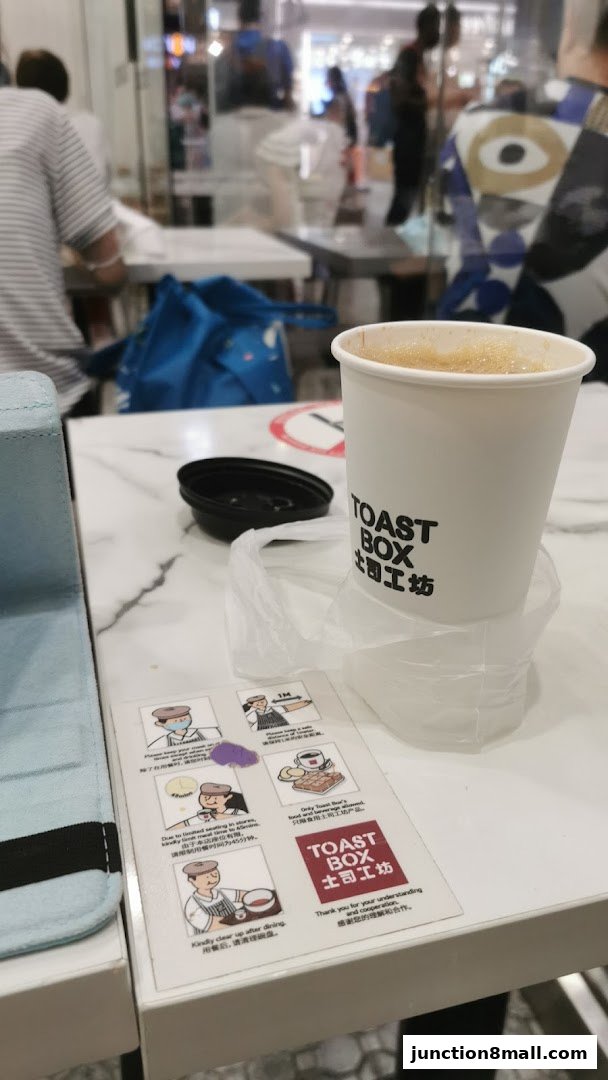 A cup of coffee from Toast Box sits on a table with safety instructions.