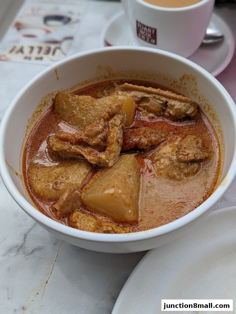 A bowl of curry with chicken and potatoes, served with a cup of tea.