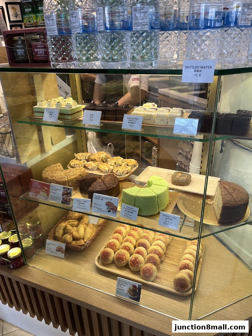 A display case filled with various cakes, pastries, and bottled water at Toast Box.