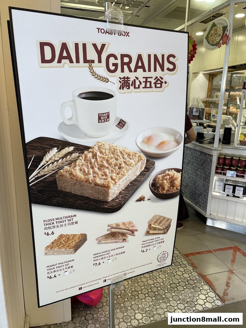 A promotional poster for Toast Box's Daily Grains menu featuring various toast sets and coffee.