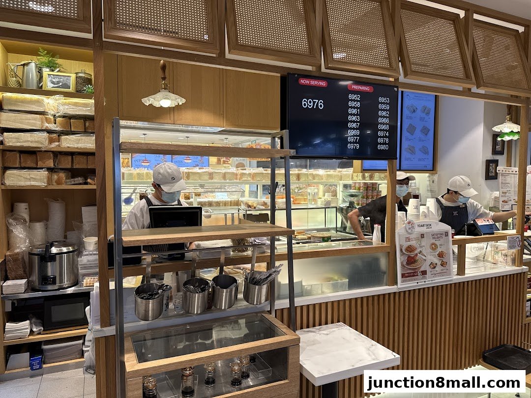 Interior view of a Toast Box shop with staff preparing orders and shelves stocked with bread.