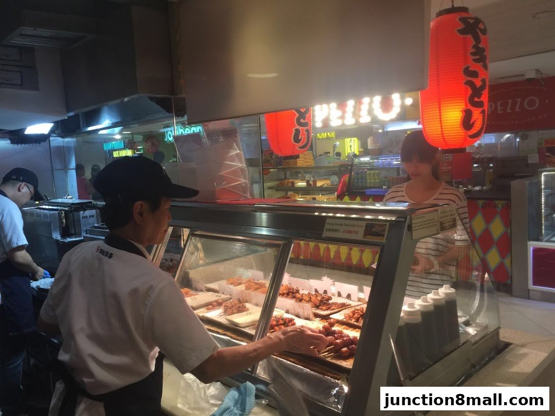 Staff serving food at a Japanese yakitori stall with red lanterns.