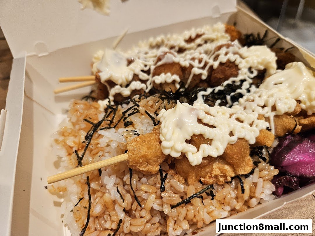 A close-up of a takeaway box filled with rice, skewered fried chicken, and mayonnaise.