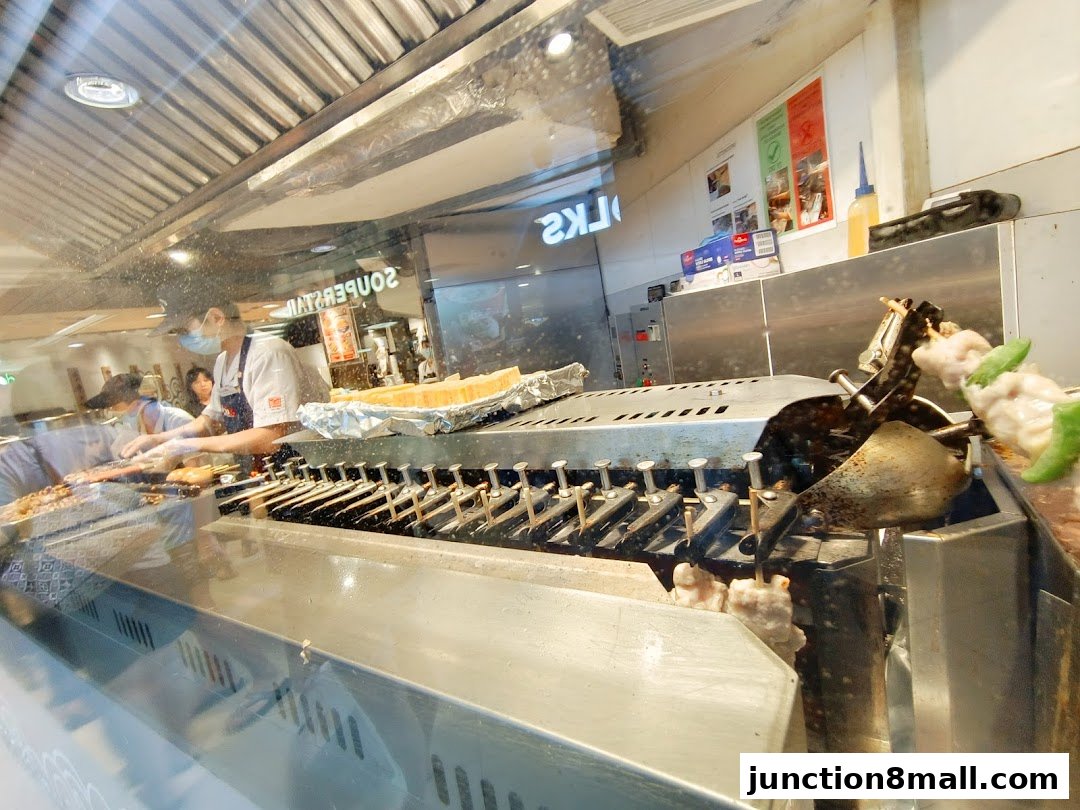 Staff preparing skewers at a food stall with a grill and various ingredients.