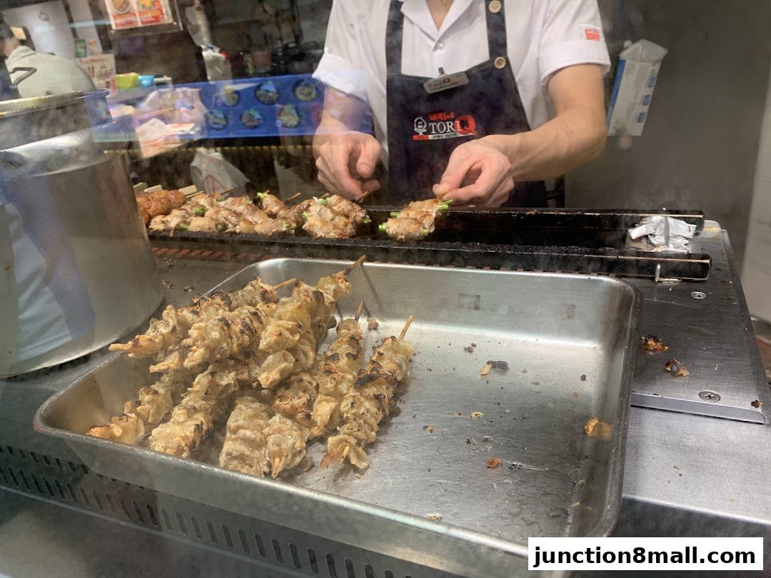 A chef prepares grilled skewers at a Tori-Q restaurant counter.