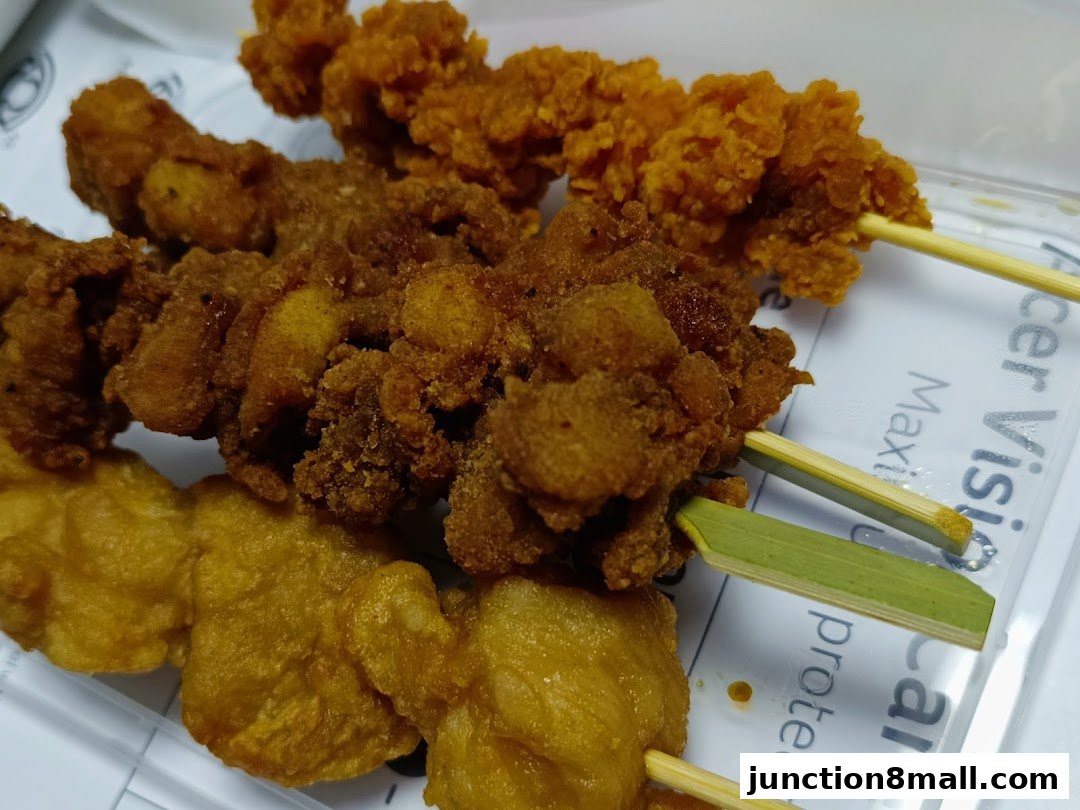 Close-up of three skewers of crispy fried chicken pieces in a clear container.