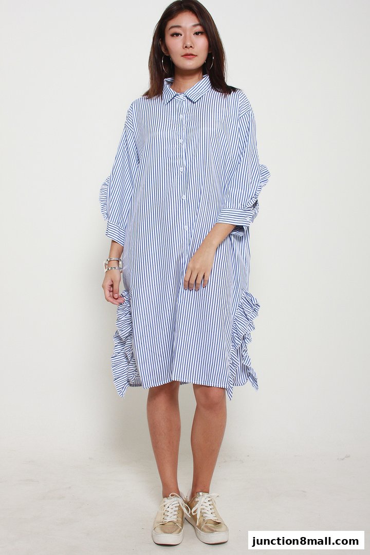A woman models a blue and white striped dress with ruffled details and gold sneakers.