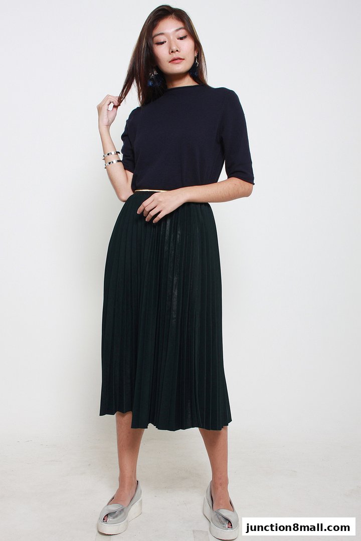 A woman models a dark blue top and a dark green pleated skirt with silver accessories.